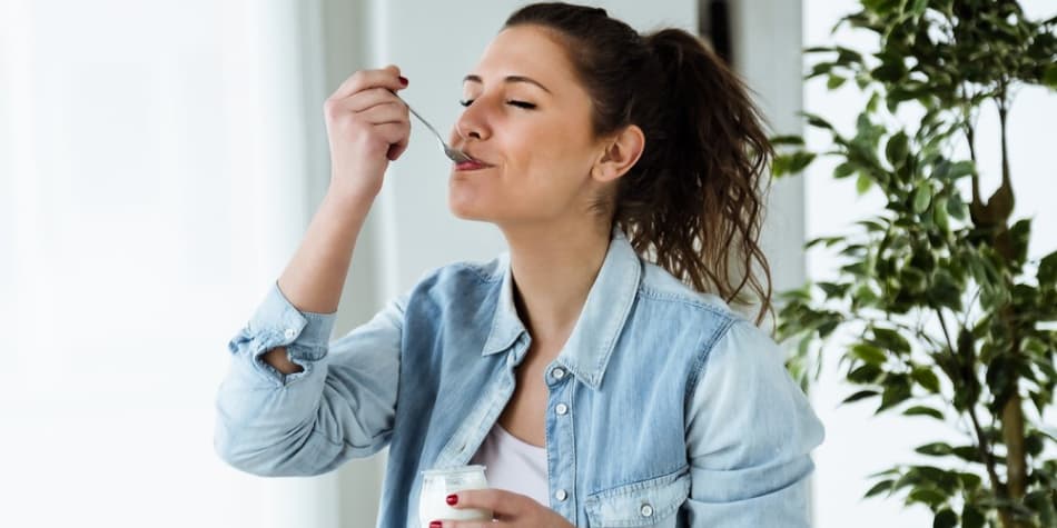 A young woman eats yogurt to help heal her gut.