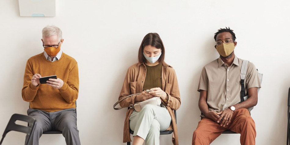 A group of people of diverse ages and ethnicities sitting in a hospital waiting room.