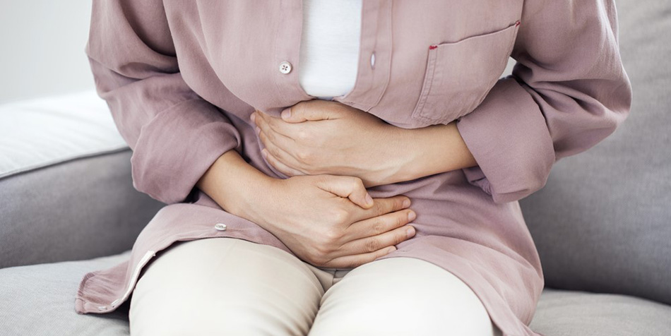 A woman holds her abdomen and leans forward, showing she is in pain.